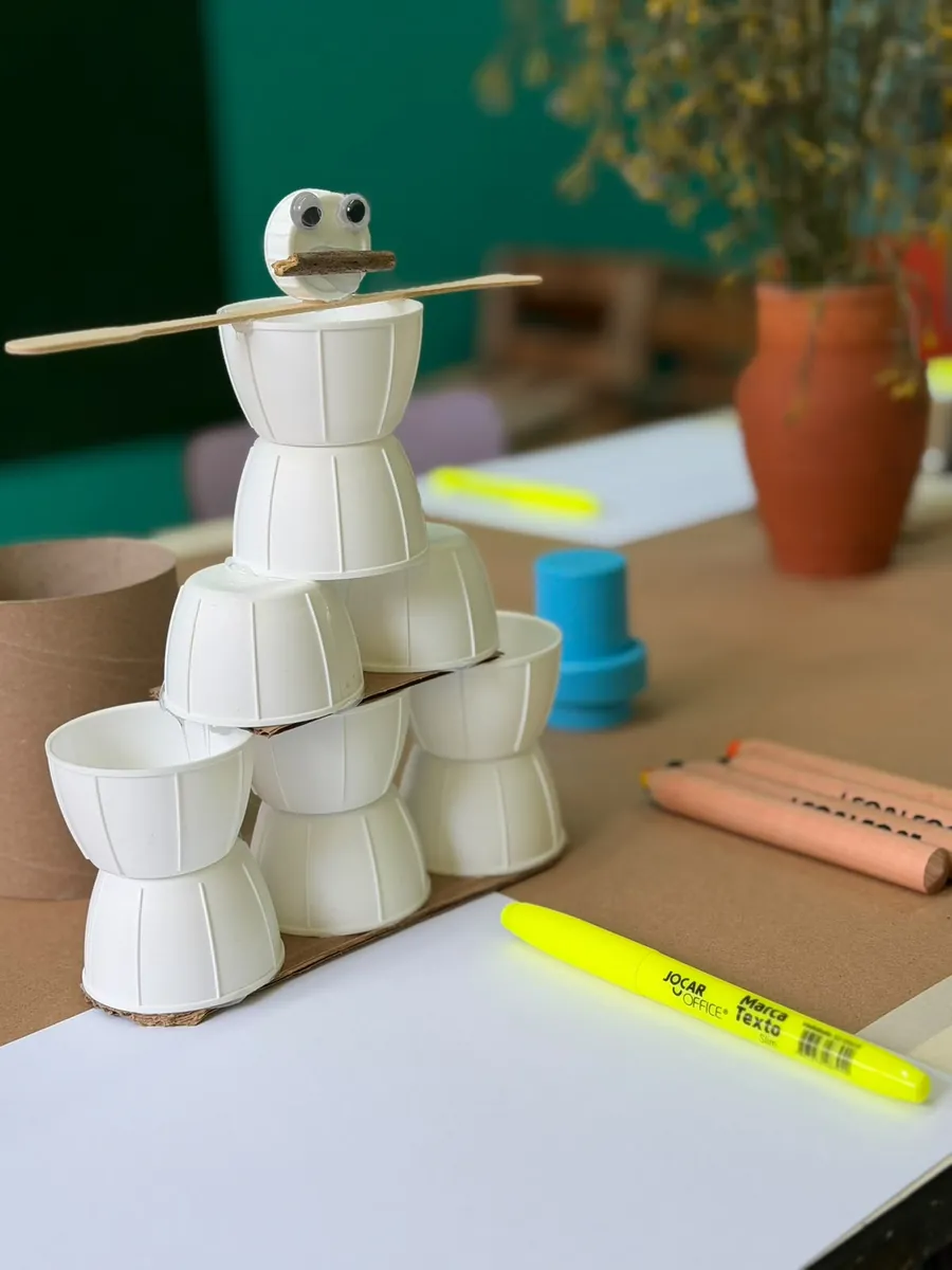 Brinquedo criado com copos de papel, palitos e materiais do dia a dia sobre a mesa de criação do ITB